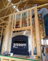 A man standing on a ladder, working on the construction of a wooden room with a fireplace, illustrating a construction or renovation project